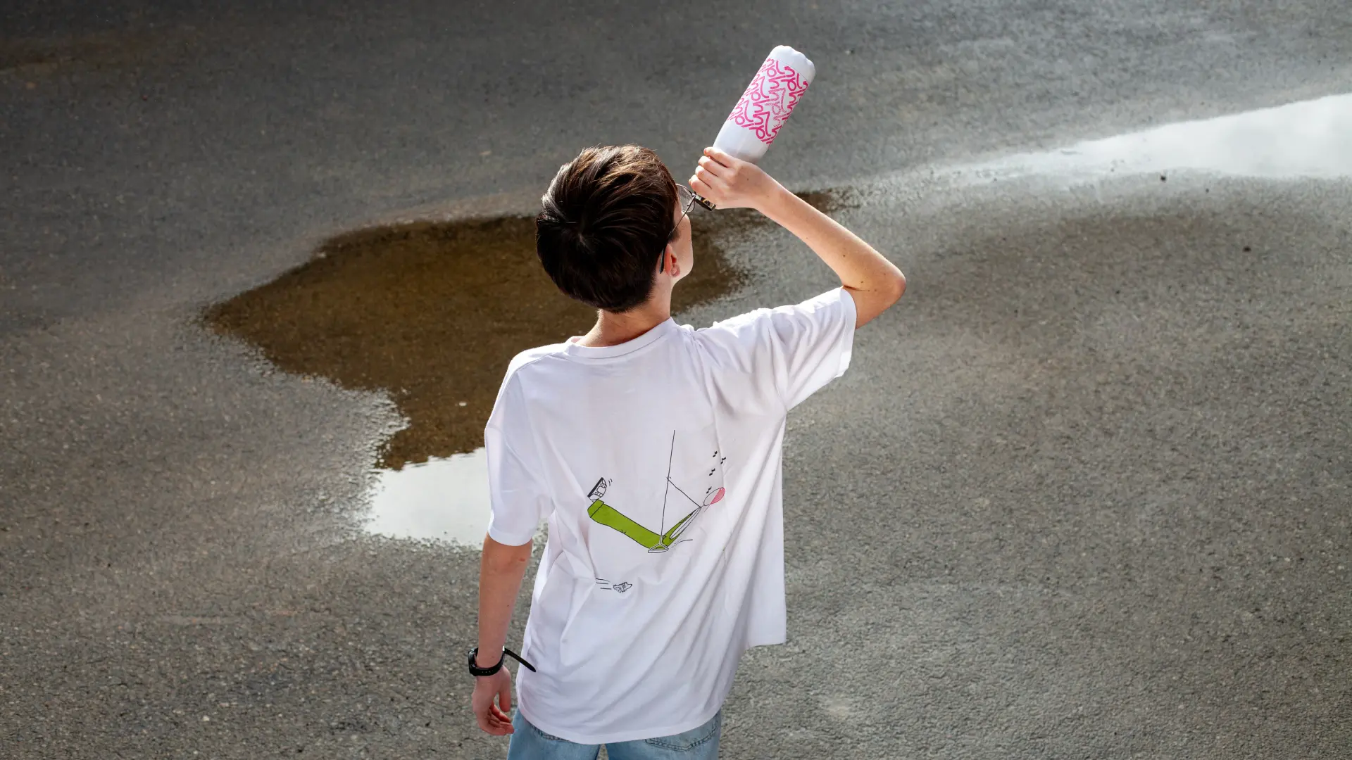 Photographie de dos d'un t-shirt illustré porté dans la rue, avec une gourde personnalisée